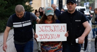 Полицейские ведут активистку, держащую плакат с надписью: "Анцухелидзе бессмертен!". Фото: Леван Зазадзе / Pirveli https://tvpirveli.ge/ka/siaxleebi/sazogadoeba/103394-aqtivisti-plakatit-antsukhelidze-ukvdavia-5000-larit-daajarimes